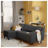 Living room with gray BRUKSVARA l-shaped sofa-bed, colorful pillows, books, plants, and a dining area with yellow walls.