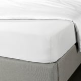 White fitted sheet on bed. Soft, silky, recycled polyester, fits 16 cm mattress.