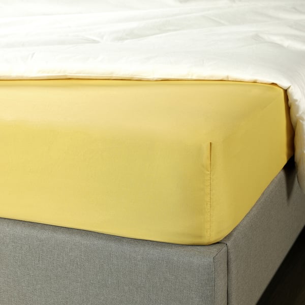A yellow fitted sheet on a bed, made from soft, silky recycled polyester, designed to fit mattresses up to 16 cm thick.
