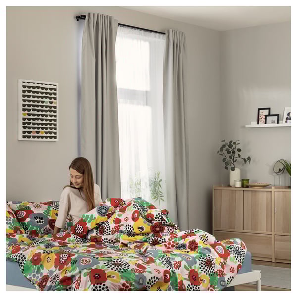 Woman on floral bed in cozy room. Bright patterns, plant, frames.