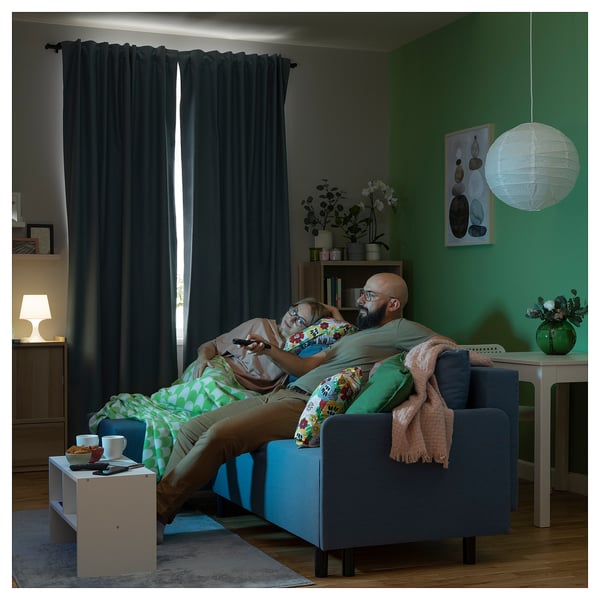 Cozy living room: dad and daughter relax on blue BRUKSVARA curtains, with green walls, wooden floor, and hanging lamp.