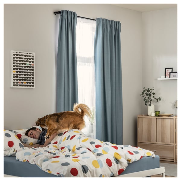 Cozy bedroom with polka dot bedding, blue curtains, dog cuddling sleeper, colorful decor, wooden cabinet, wall art.
