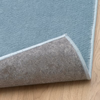 Corner of soft, lightweight blue rug on wooden floor.
