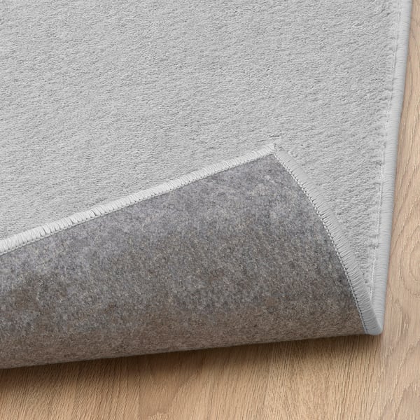 Light grey, soft, durable rug on wooden floor. Stain-resistant & cozy, perfect for living or bedroom. Anti-slip underlay needed.