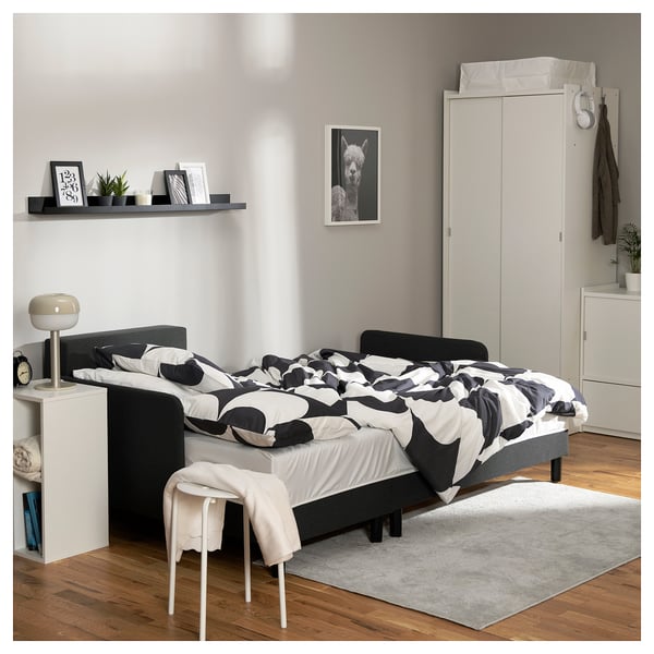 Modern bedroom with black & white patterned bedding, white rug, black nightstand, and wall decorations including a sheep poster.