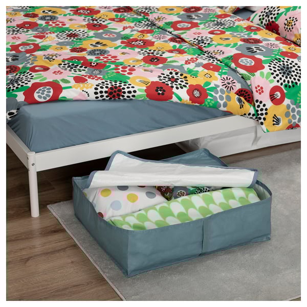 Bright blue fabric storage bin under white bed with colorful flowery bedspread.