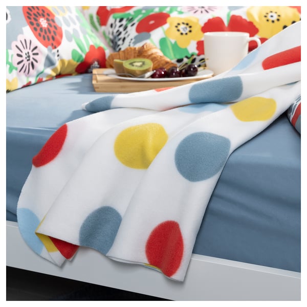 Brightly colored polka dot blanket on a floral pillow bed, with breakfast tray.