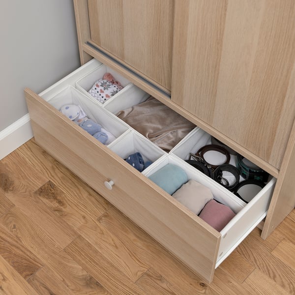 Open oak wardrobe drawer with folded clothes and accessories neatly organized in compartments.