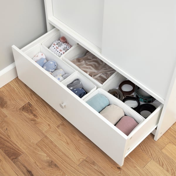 A white wardrobe with an open drawer showcasing neatly folded clothes and accessories in separate compartments.