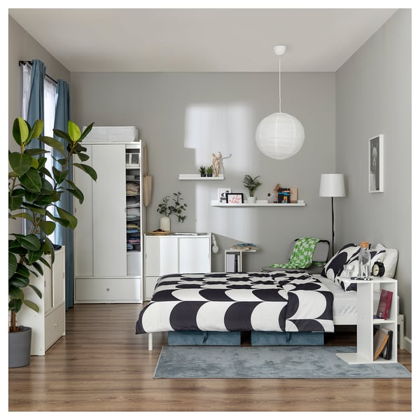 Neat bedroom with a white BRUKSVARA wardrobe holding clothes, a bed with circular bedding, and a side table against grey walls.