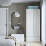 Modern bedroom with gray walls, BRUKSVARA wardrobe, mirror, dressers. Wardrobe by window, soft lamp.