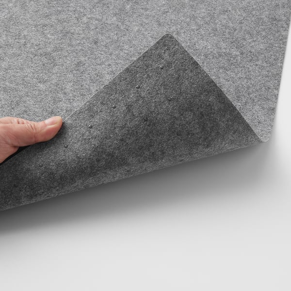 Image description: hand peeling back corner of textured gray table mat, revealing silicone dots underneath, showcasing its grip function.