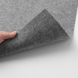 Image description: hand peeling back corner of textured gray table mat, revealing silicone dots underneath, showcasing its grip function.
