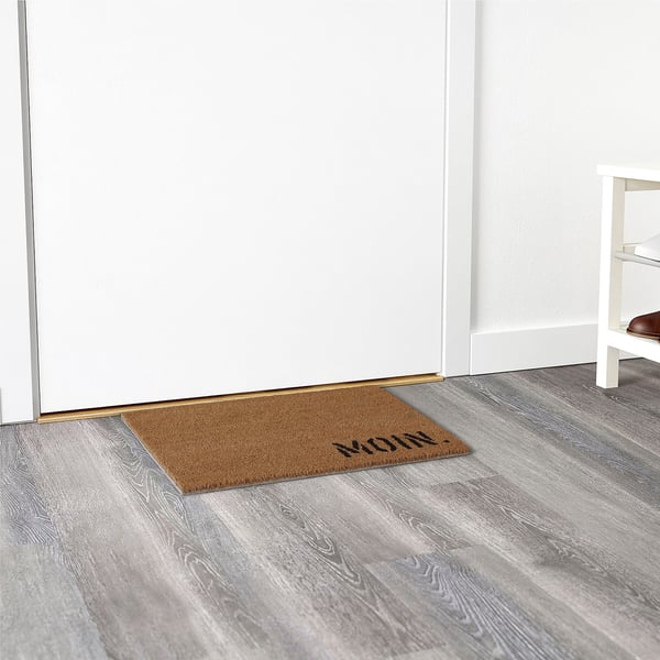 Doormat with mum text near a white door. Keeps dirt outside, placed on wooden floor.