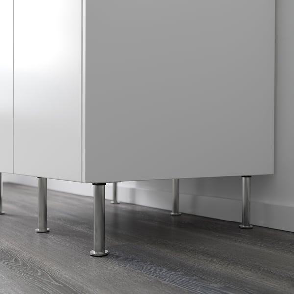 White kitchen cabinet elevated by four silver adjustable legs on dark wood floor.