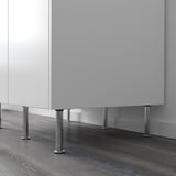 White kitchen cabinet elevated by four silver adjustable legs on dark wood floor.