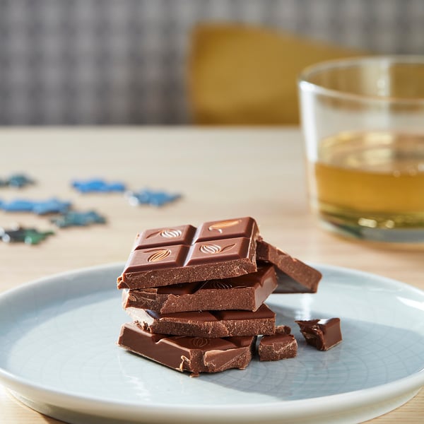 Plate of stacked dark chocolate bars next to a glass of amber liquid.