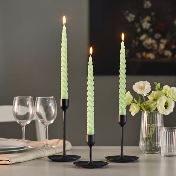 Table set with lit, green spiral candles in black holders; glasses, plates, and flowers nearby.