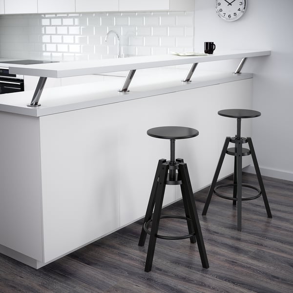 Modern kitchen with 2 DALFRED stools. Adjustable height, mugs & papers on counter, white backsplash.