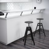 Modern kitchen with 2 DALFRED stools. Adjustable height, mugs & papers on counter, white backsplash.