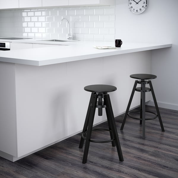 Two black DALFRED bar stools adjustable in height by counter with white wall and clock.