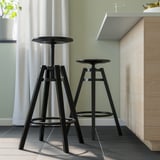Two adjustable bar stools with round seats and black metal frames next to a wooden bar.