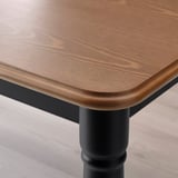 Close-up of a wooden dining table with a dark metal leg, showcasing its polished wooden top and sturdy design.