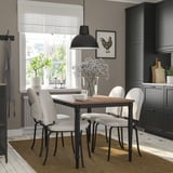 Modern dining set with black metal legs & wooden top, four white chairs, hanging light, gray walls, large window.