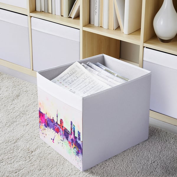 White storage box with colorful abstract art on shelf, holding papers.