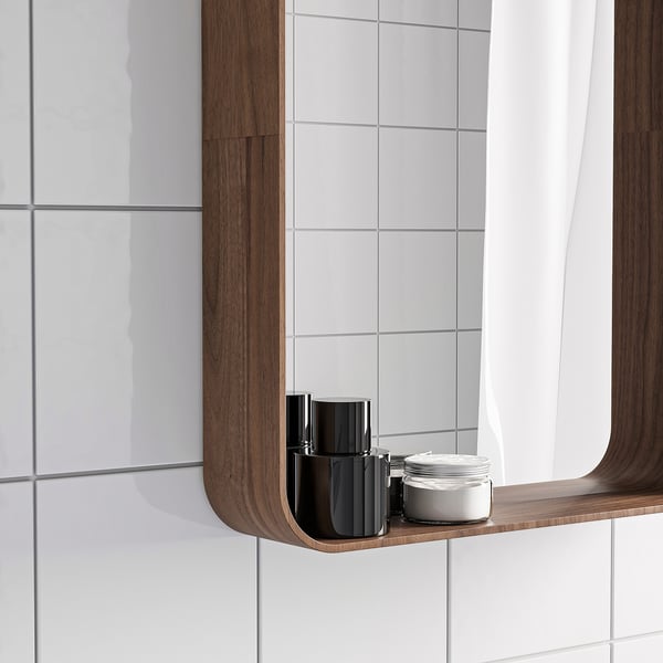 Bathroom mirror with walnut shelf, holding black bottle and white jar.