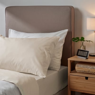 Bed with DVALA beige cotton pillowcases, wooden nightstand holding clock and plant.