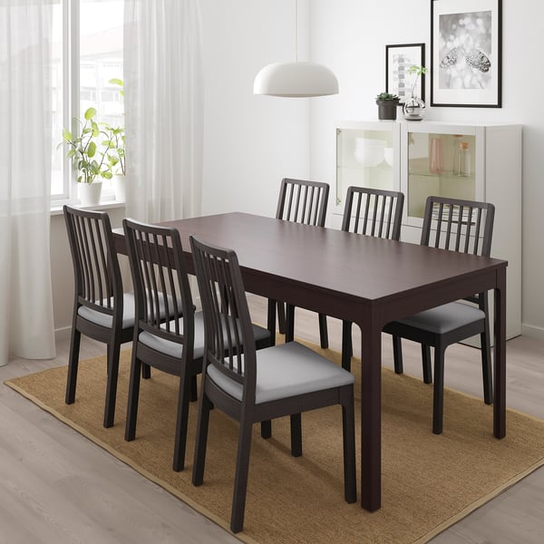 Dark brown extendable dining table with 6 light grey cushioned chairs, rug, sideboard, large window.