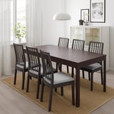 Dark brown extendable dining table with 6 light grey cushioned chairs, rug, sideboard, large window.
