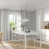White dining table with clear chairs, two pendant lights, beside a window. Fits six.