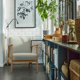 Gray EKENÄSET armchair against white wall with bookshelf, lamp, and plant.