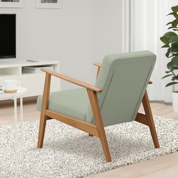 Armchair: EKENÄSET in green fabric & wood, on speckled rug near side table with mug, tv, and plant.