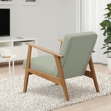 Armchair: EKENÄSET in green fabric & wood, on speckled rug near side table with mug, tv, and plant.