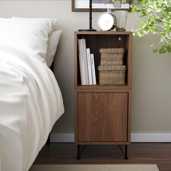 Modern brown nightstand with open & closed storage, beside bed, holds books & boxes.