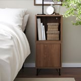 Modern brown nightstand with open & closed storage, beside bed, holds books & boxes.