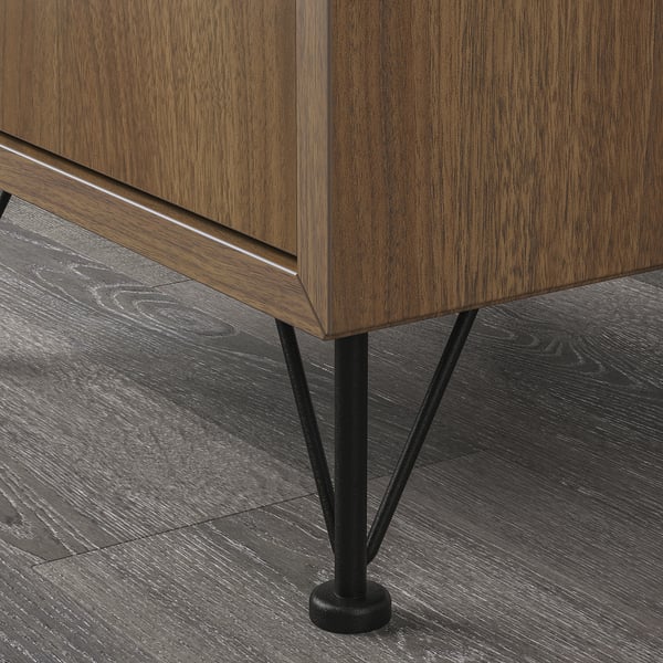 A close-up of a modern wooden cabinet with sleek metal legs. Dark wood grain and black metal details are prominent.