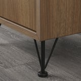 A close-up of a modern wooden cabinet with sleek metal legs. Dark wood grain and black metal details are prominent.