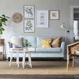 Cozy living room with light blue sofa, yellow pillows, rug, side table, wicker chair, art gallery, and wall hanging.