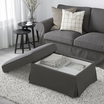 Image description: living room with grey EKTORP sofa and ottoman. Ottoman has a lift-up seat revealing storage space with blanket and book inside.