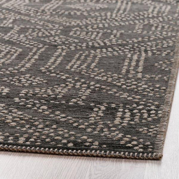 Dark patterned rug with textured design on wooden floor.