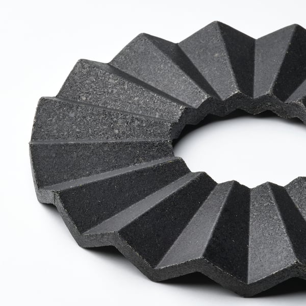 A black, circular trivet with angular, overlapping segments, crafted from compressed bamboo, exuding a modern aesthetic and robust quality.