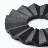 A black, circular trivet with angular, overlapping segments, crafted from compressed bamboo, exuding a modern aesthetic and robust quality.