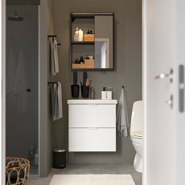Modern bathroom featuring white ENHET vanity, mirror, and toilet. It includes sleek black accessories and a gray shower cubicle.