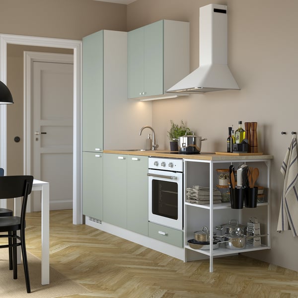 Modern kitchen with light green ENHET cabinets, white oven, open shelves with cookware, countertop appliances, potted plant, and area rug.