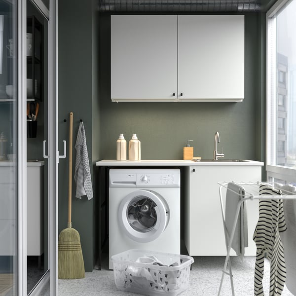 Small white laundry room with cabinets, washing machine, laundry basket, and drying rack.