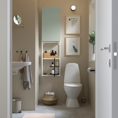 Beige bathroom with grey-green cabinet & shelves beside toilet.